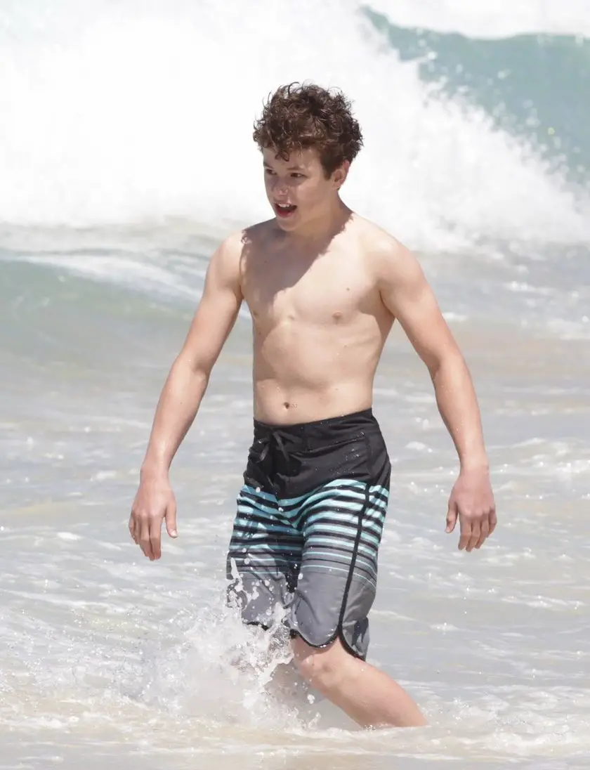 Nolan Gould shirtless on the beach going into a wave.